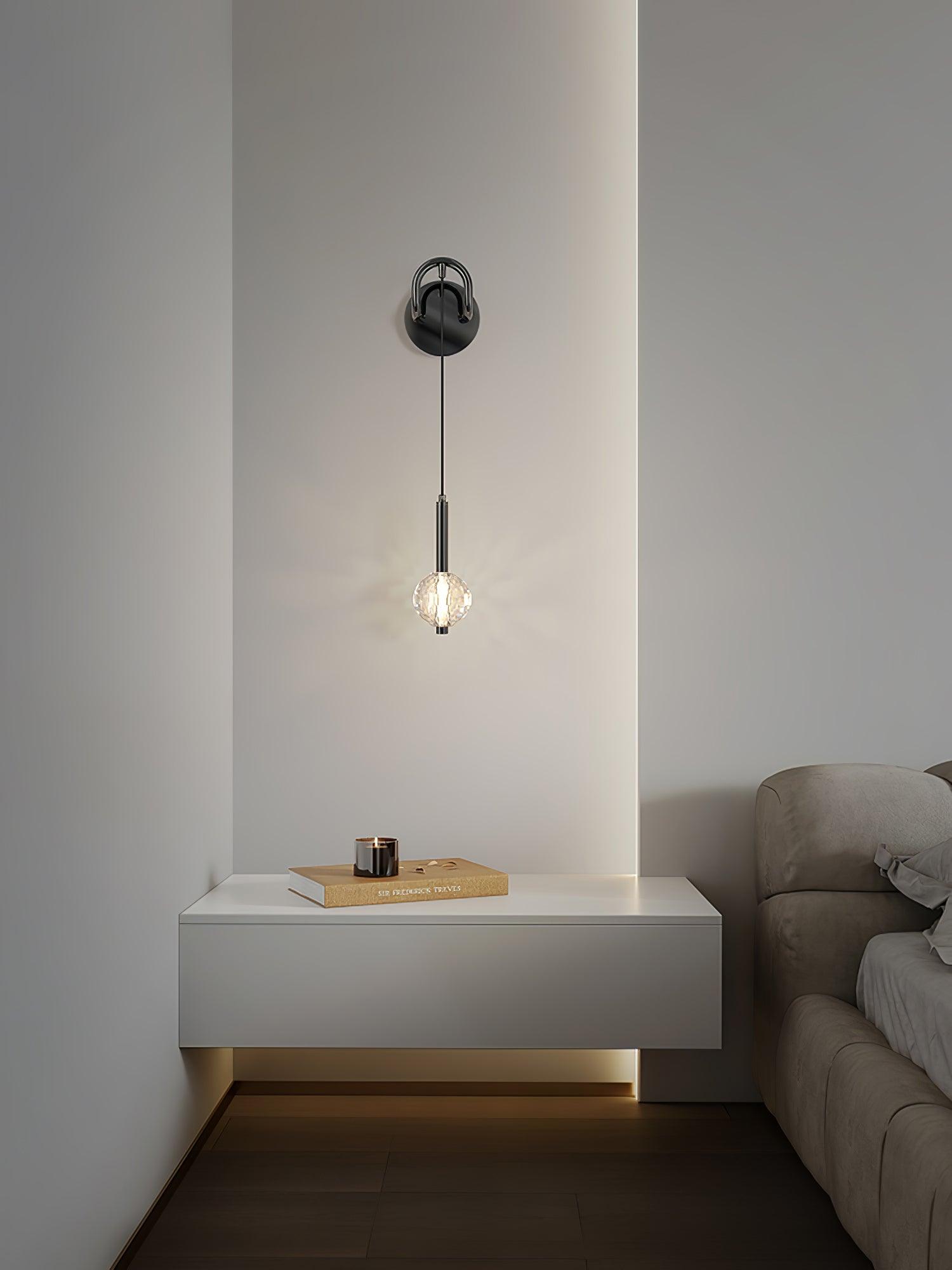 Lit glass globe wall light above a floating white bedside cabinet with a gold-coloured book and dark cup