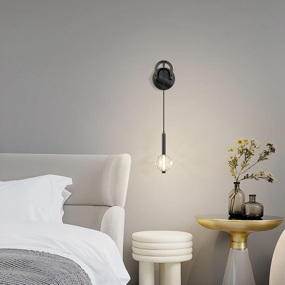 Front-view hanging globe wall light beside a white upholstered bed, gold round table with vases and a white stool