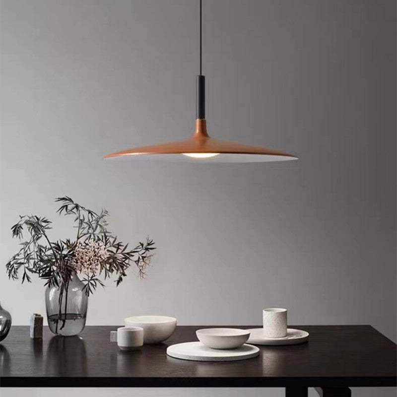 Red-brown shallow dome pendant above a dark dining table with white bowls and a vase