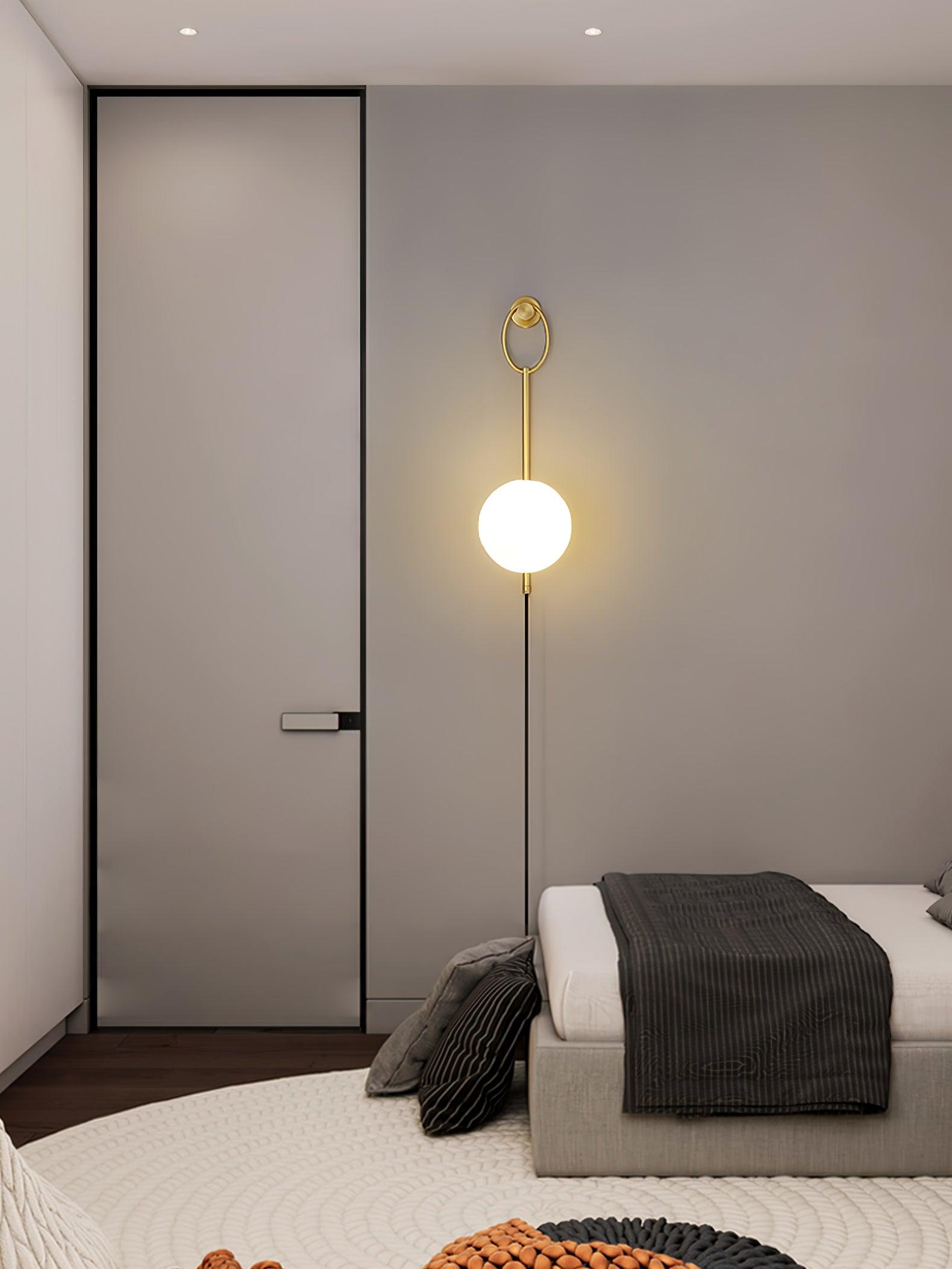 Tall ring-and-globe wall light beside a bed
