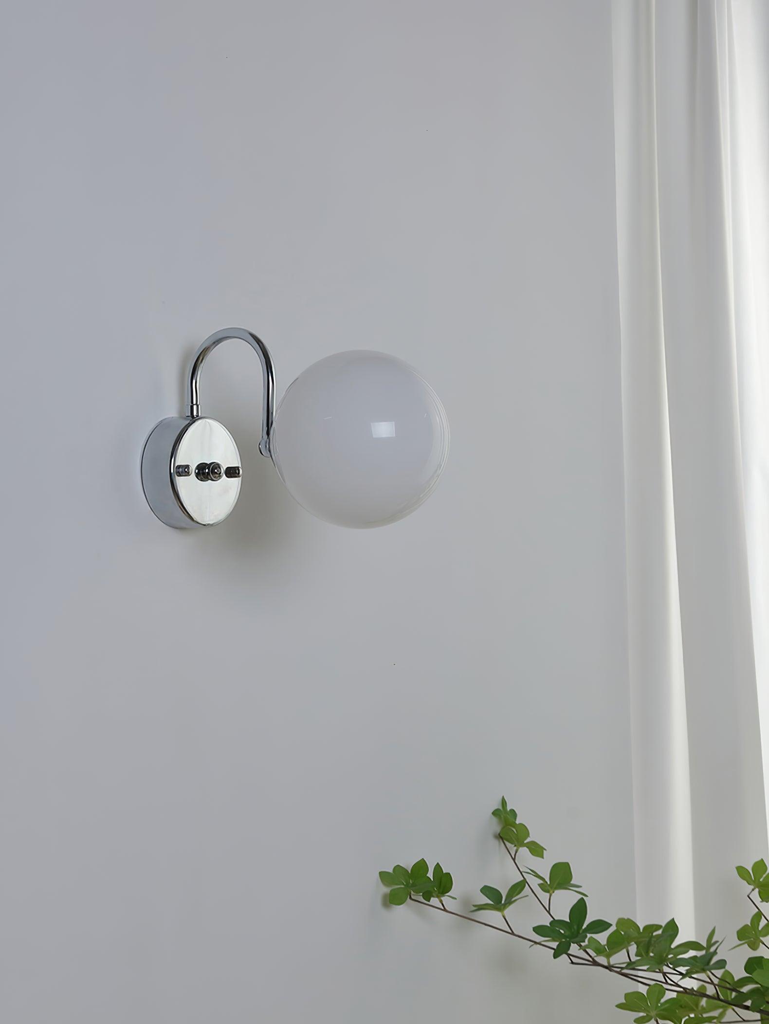 Unlit white globe at right of a reflective round plate, with upper curved arm, white curtain and greenery below