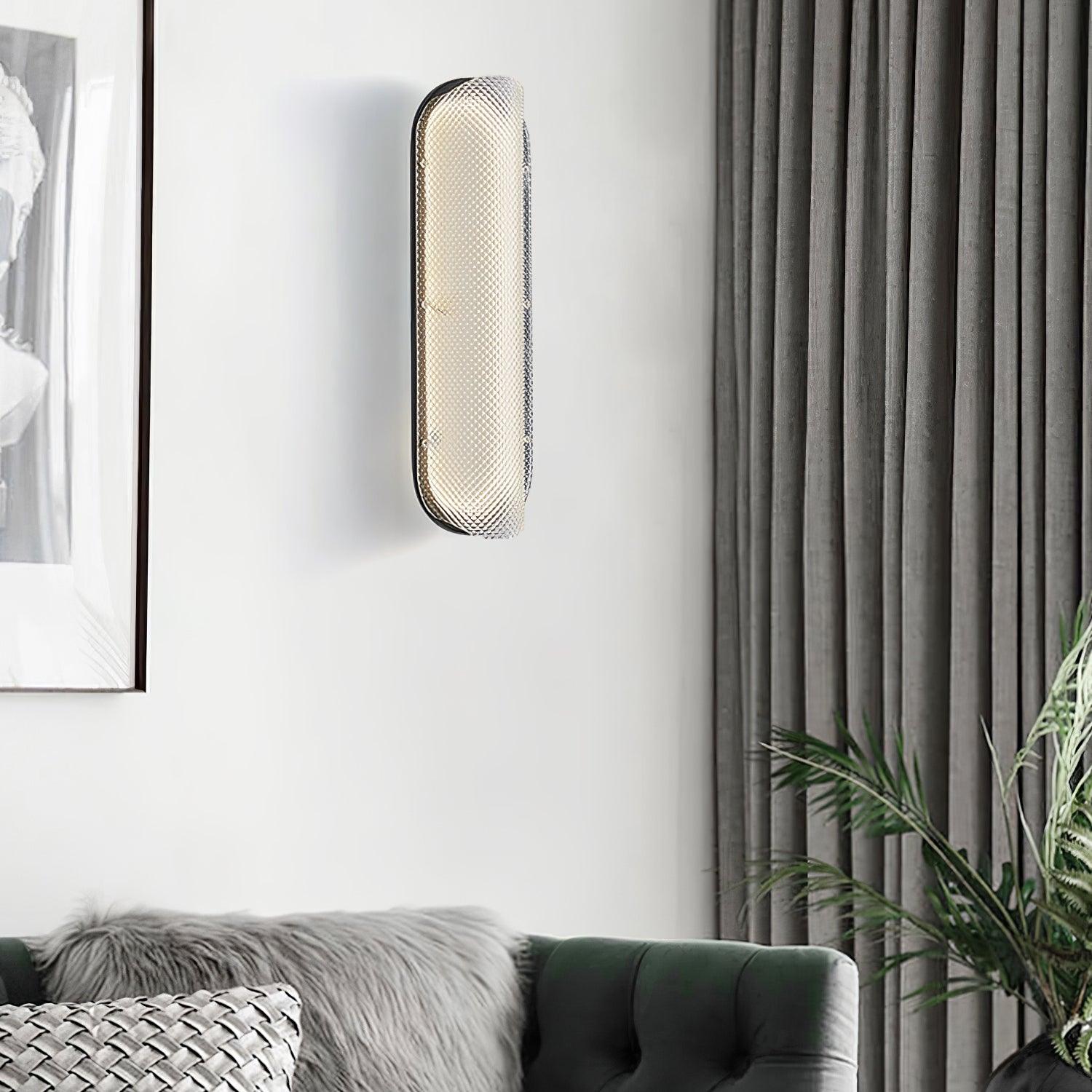 Angled lit Vale glass wall light above a green sofa beside a fluted wall panel, picture and plant