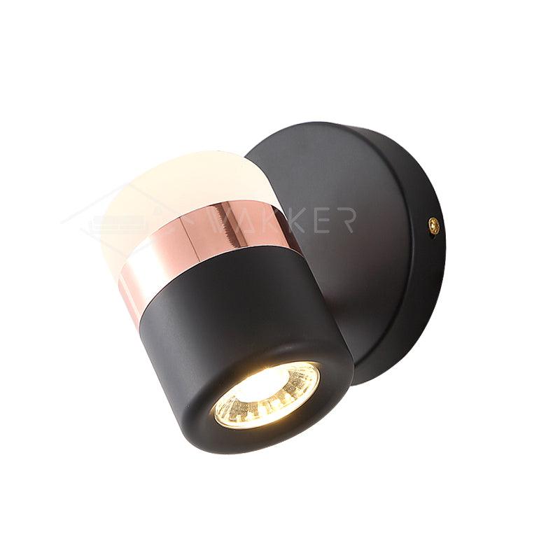 Black cylindrical wall light with copper-coloured band angled beside a round black wall plate
