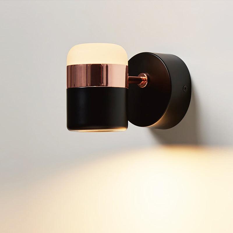 Upright black and copper-coloured cylinder wall light illuminating the wall below