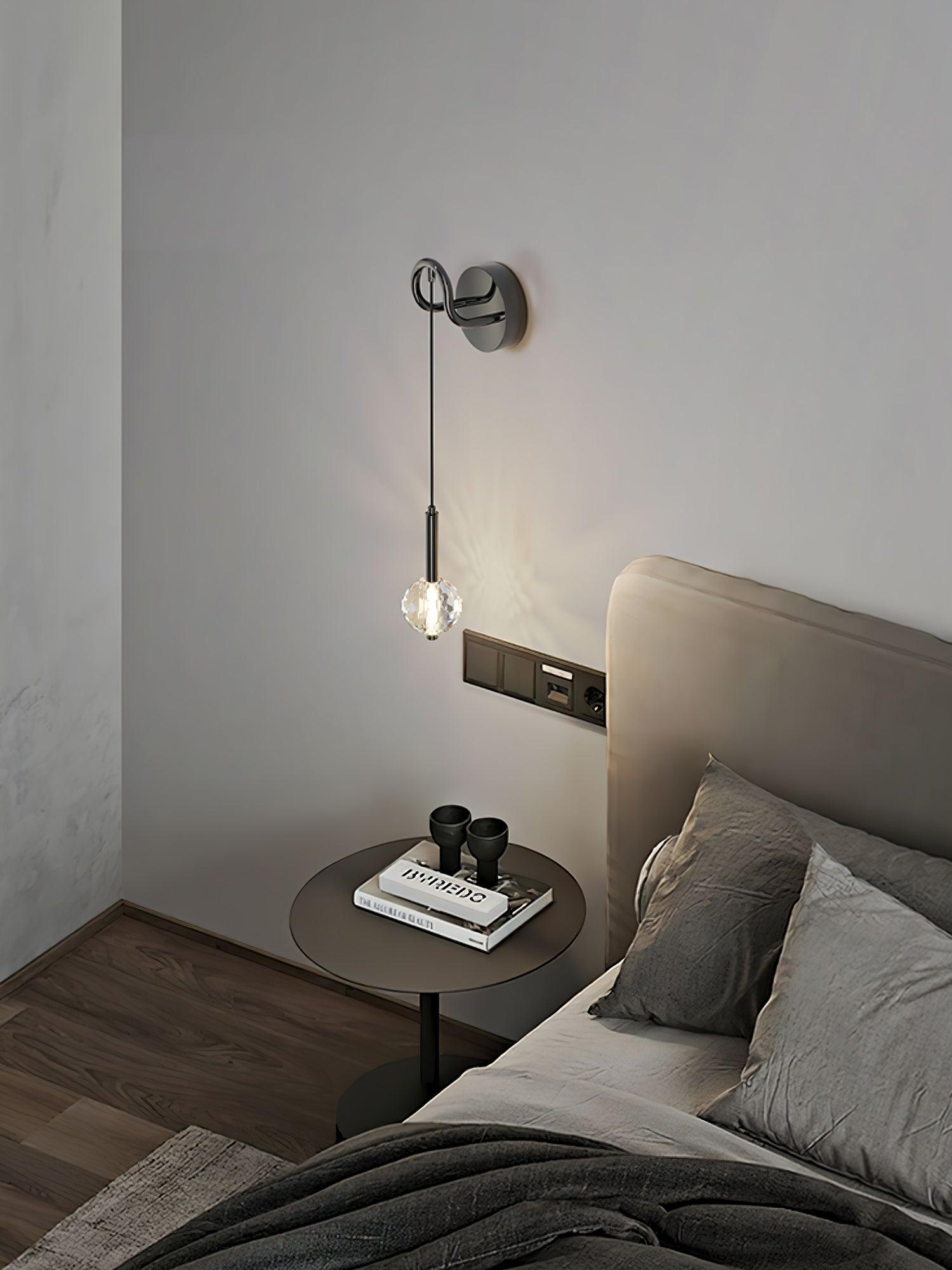 Angled bedside wall light with glowing faceted globe, beige headboard, separate switch panel and round table with books
