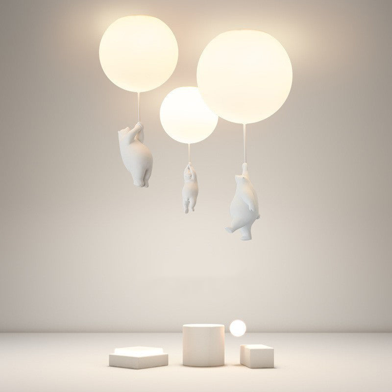Three lit Fateh balloon globes and white bear figures above geometric display blocks against a beige backdrop.