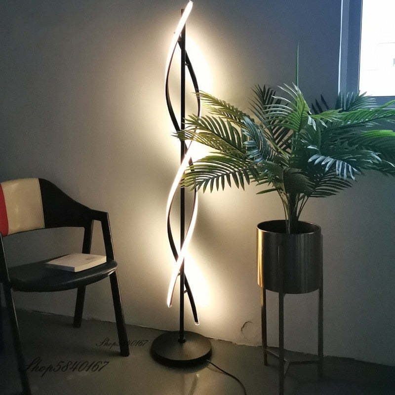 Black Louise floor lamp beside a chair and tall plant, with crossed strips lighting the wall