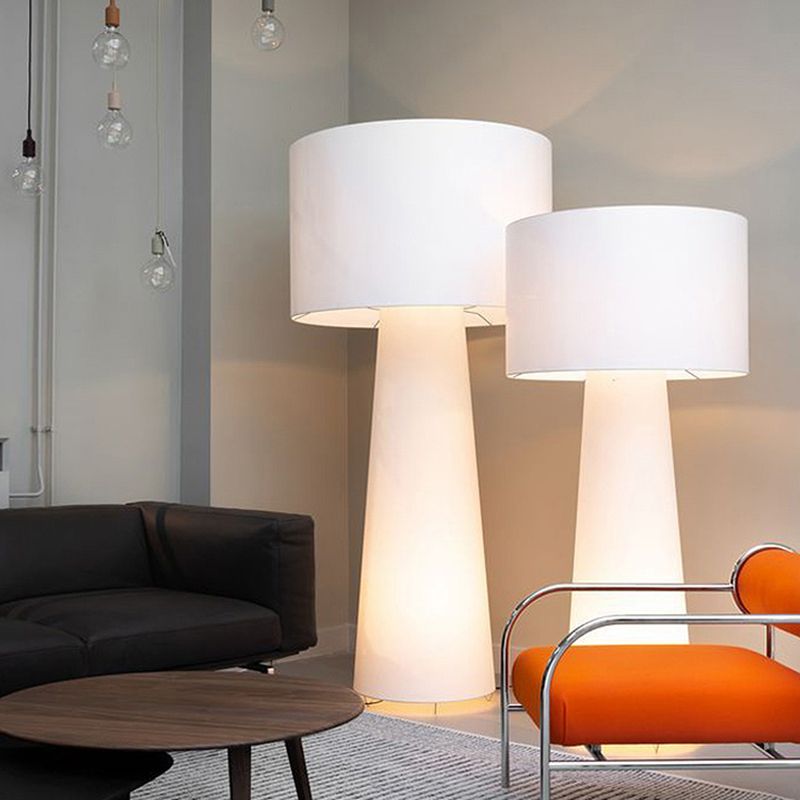 Two glowing drum-shade floor lamps beside a black sofa, orange chair and round table, with pendant bulbs in the background