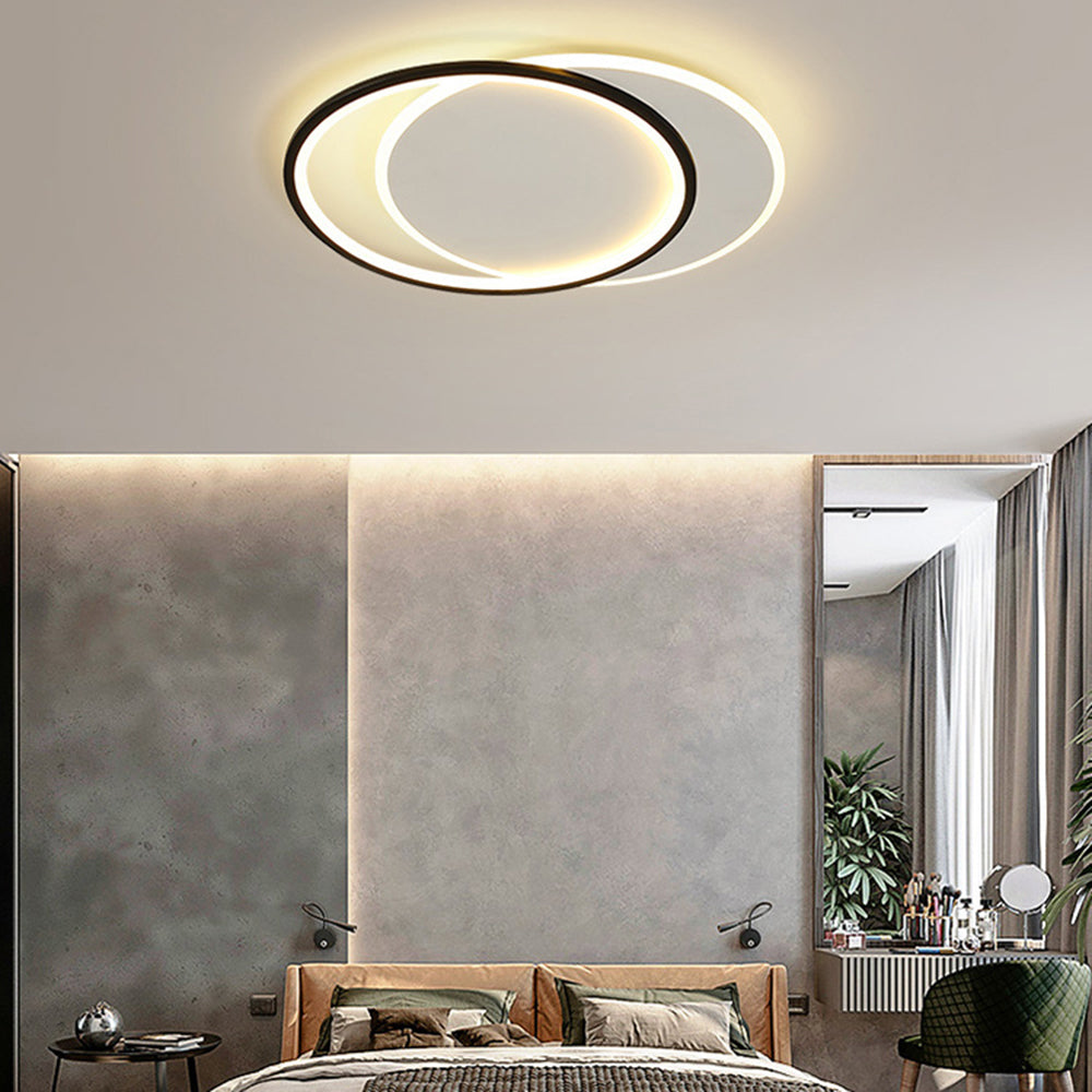 Round Quinn ceiling light above tan upholstered bed and green pillows, with grey wall panels, black reading lights and tall mirror.