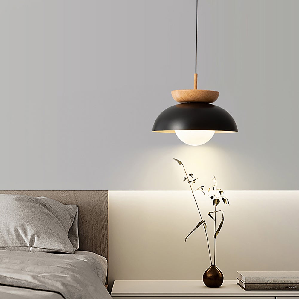 Lit black dome pendant above a bedside console with vase and books beside a grey upholstered bed