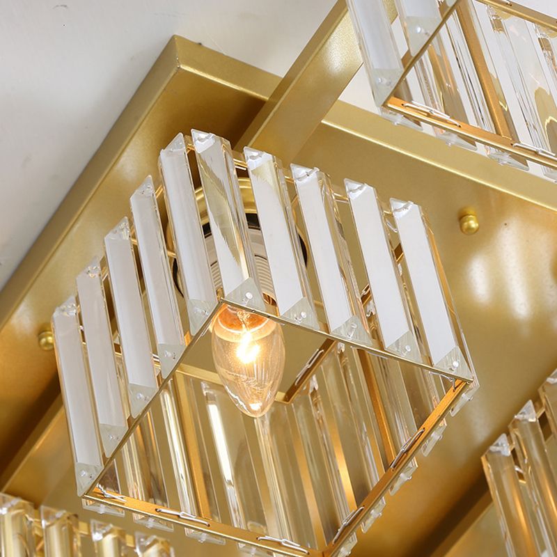 Lower-side close-up of a gold-toned Kristy cube shade, clear strips, attachment tabs, lit candle-shaped example bulb and canopy.
