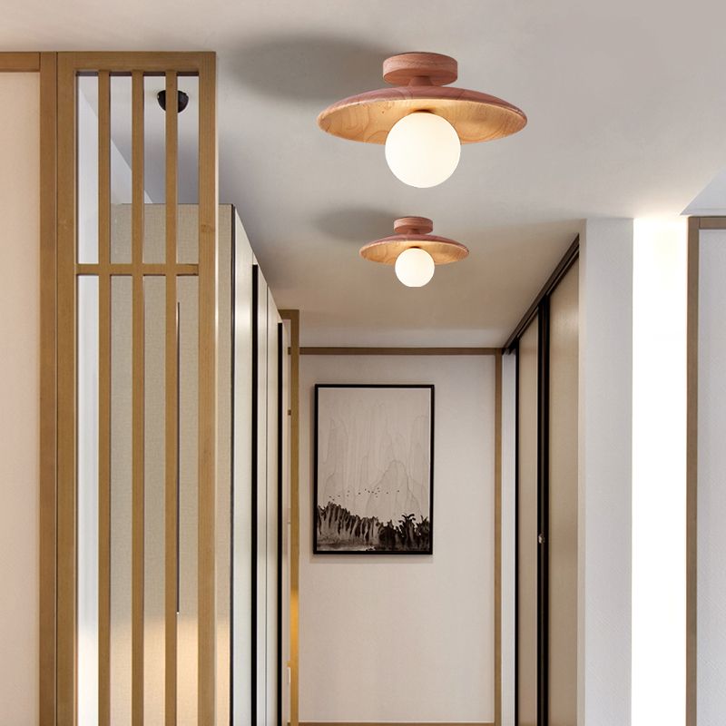 Two light wood-tone Carins disc ceiling lights with white globes in a corridor beside vertical wood slats and black-framed mountain artwork.