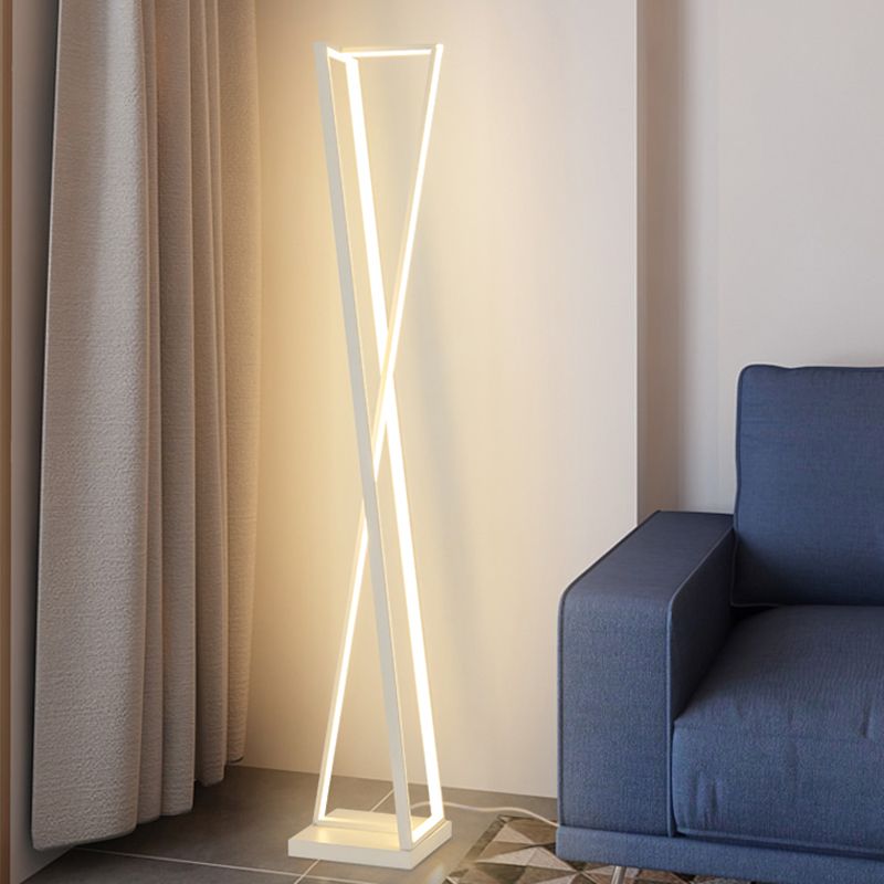 White crossed-triangle floor lamp with a lit frame beside beige curtains and a blue armchair on a patterned rug