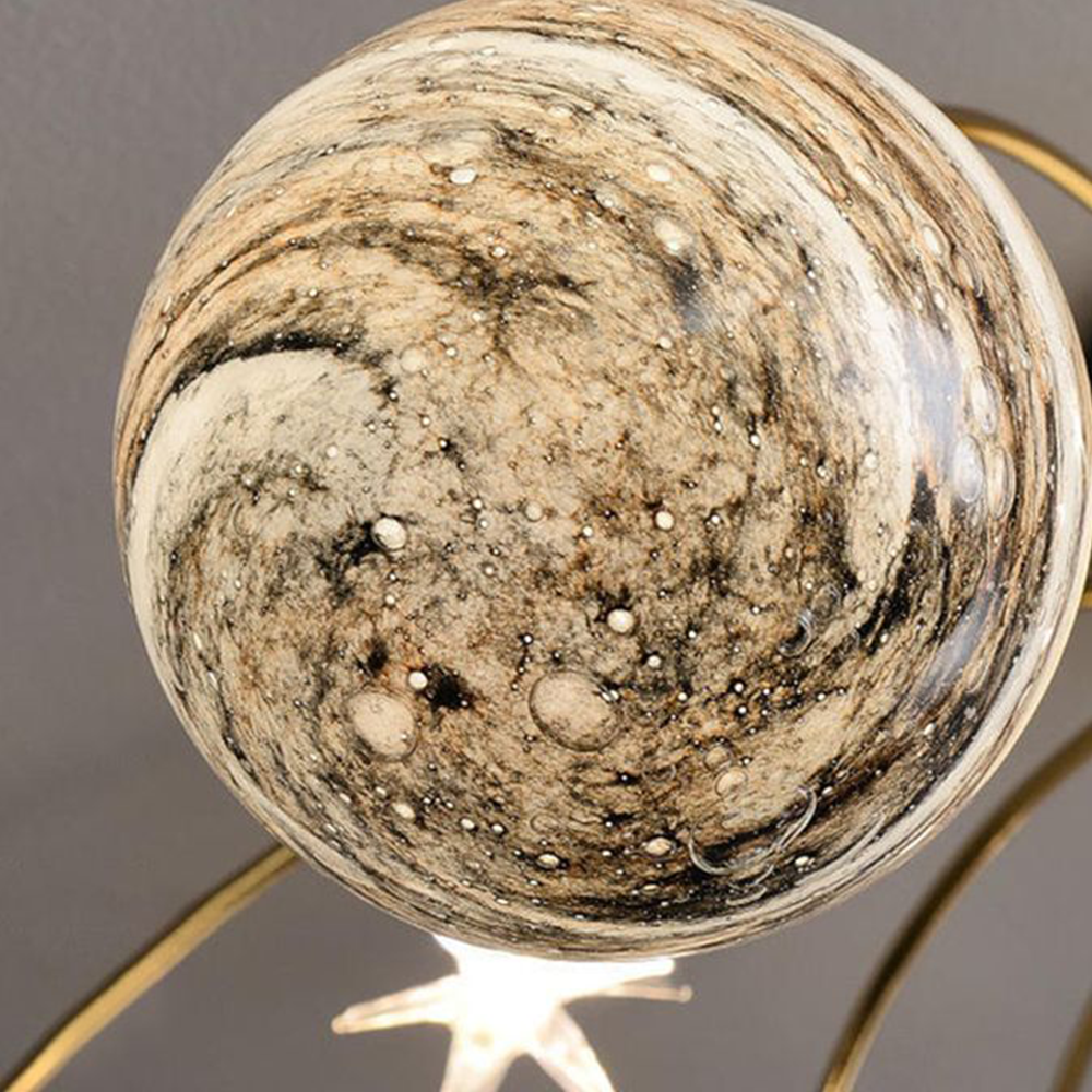 Close-up of an Elif tan glass globe with dark swirled patterns, small surface dots, a gold-toned arm and part of a bright star detail.