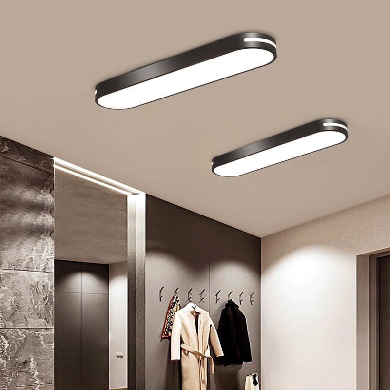 Two lit black Quinn fixtures with bright side slots above a tall mirror and wall hooks holding coats, beside a stone wall.