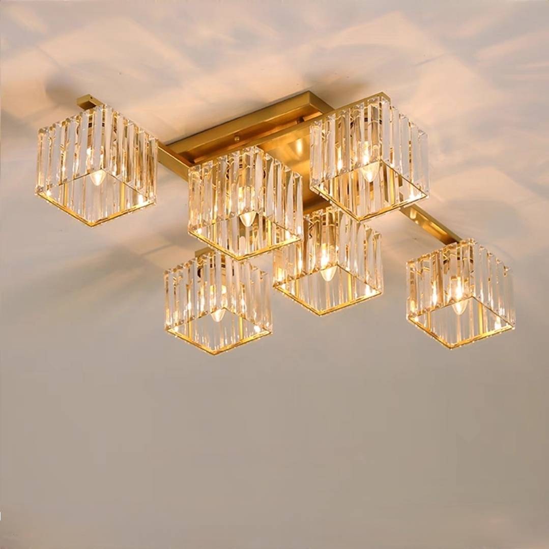 Close fixture view of six gold-toned Kristy cube shades, clear vertical strips, open square lower frames and lit example bulbs.
