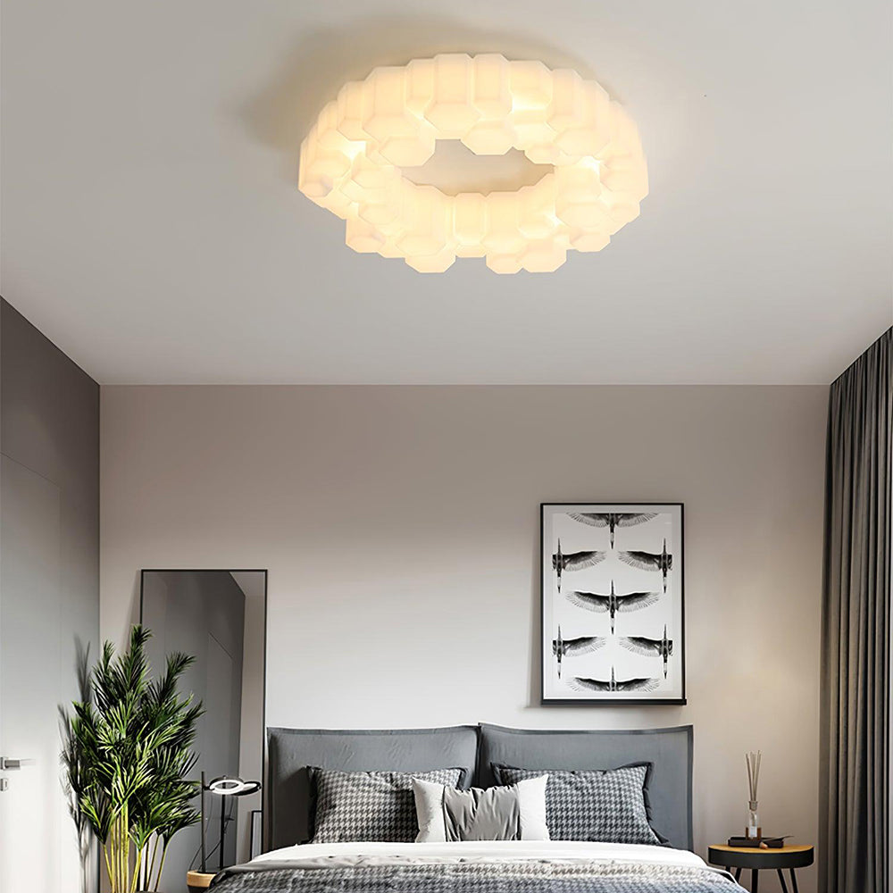 Warmly lit Quinn above a gray bed with bird artwork, a leaning mirror, tall plant, patterned pillows and a round side table.