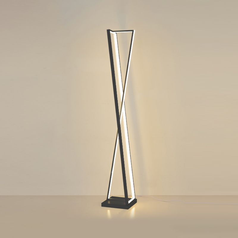 Black crossed-triangle floor lamp with warm-looking strips and a trailing cable against a beige wall and floor