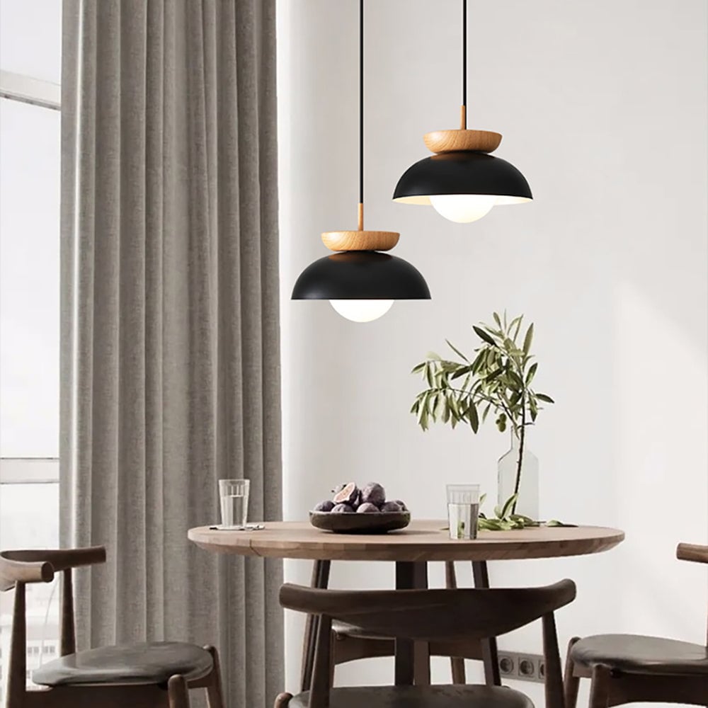 Two black wood-crowned pendants above a round wooden dining table with fruit, glasses and leafy branches