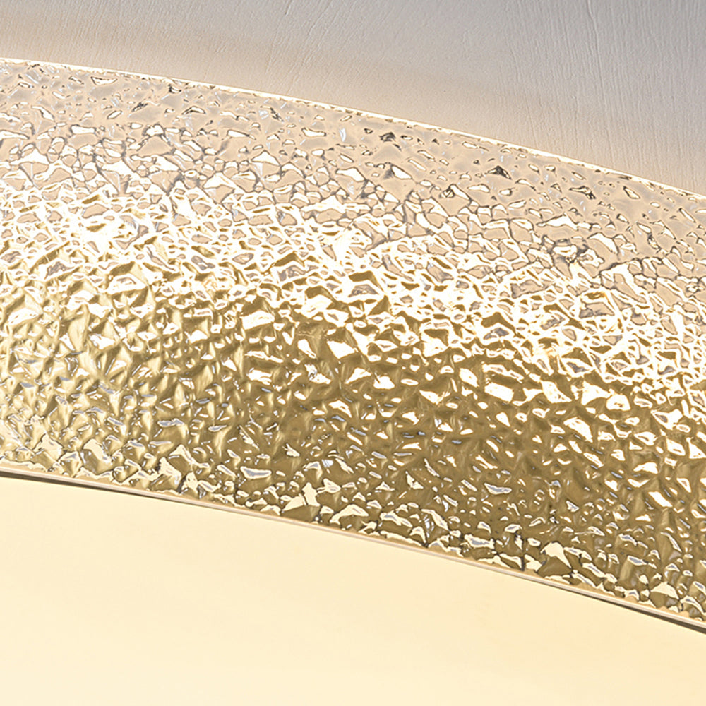 Close-up of the clear textured outer band, gold-toned surface behind the glass and pale central diffuser edge beneath the ceiling.
