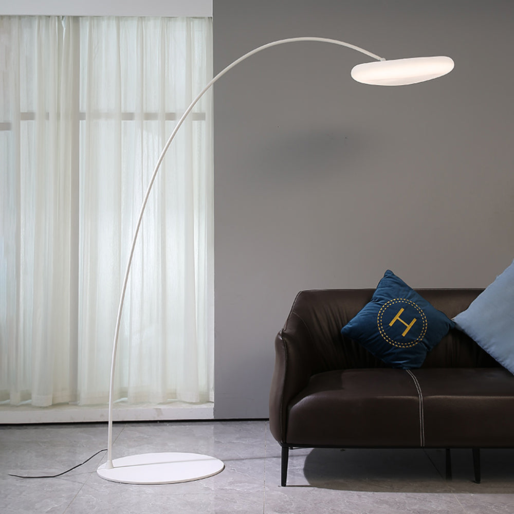 White Minori arc floor lamp beside a dark armchair and sheer curtains.