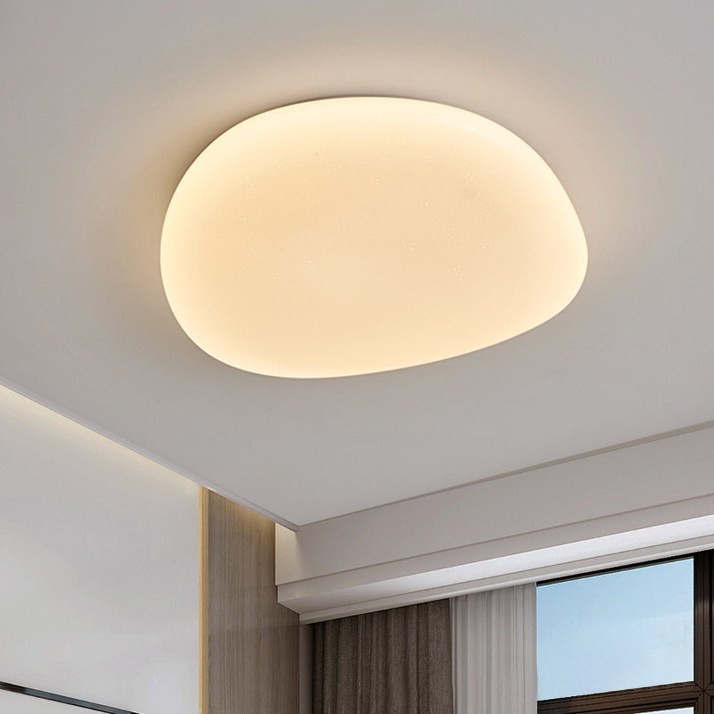 Installed Quinn pebble ceiling light near ceiling cove, wood trim, grey curtain and dark window frame.