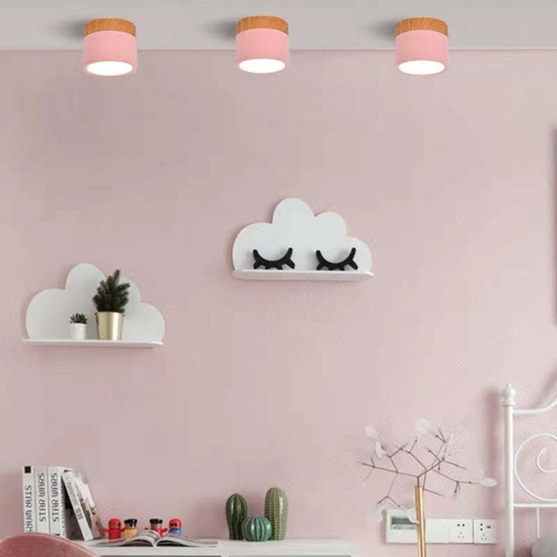 Three pink Morandi ceiling cylinders above cloud shelves, books, plants and a white bed frame in a pink room.