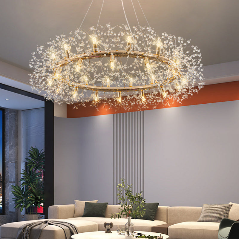 Large Lili crystal ring above a white sectional sofa and coffee table, with tall windows, green plants and a gray-orange wall.