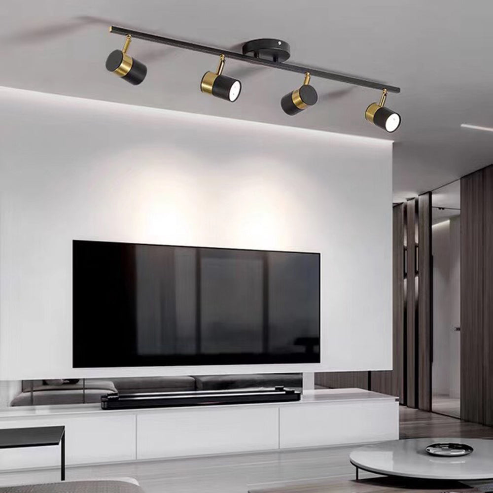 Four black and gold-tone Evette spotlights above a television and white media cabinet, with grey curtains and a round coffee table.