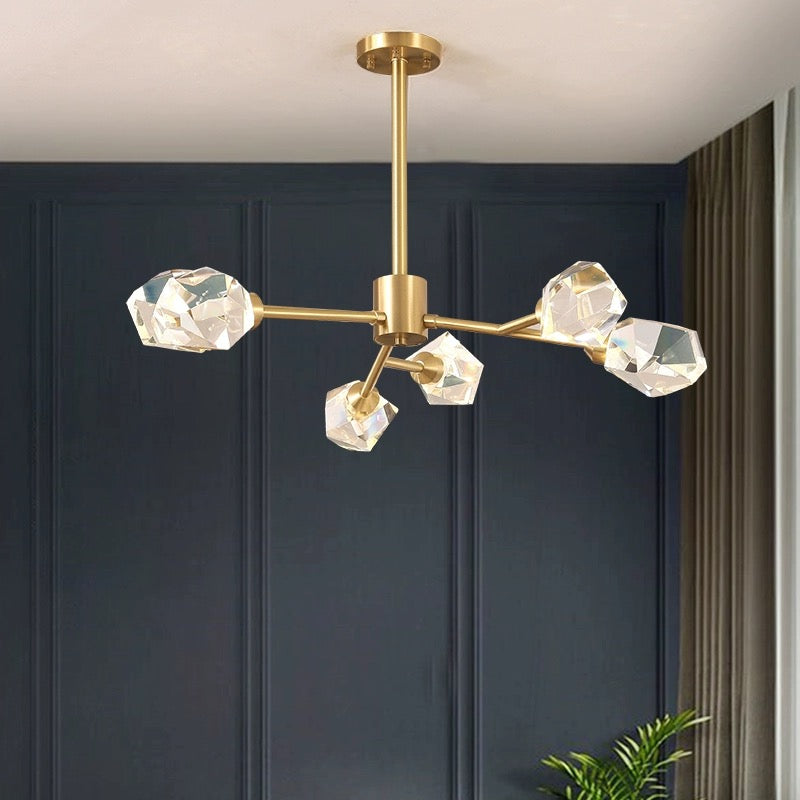 Kristy 6-light option with gold-tone branching arms and clear faceted elements against blue panelling, gray curtains and foliage.