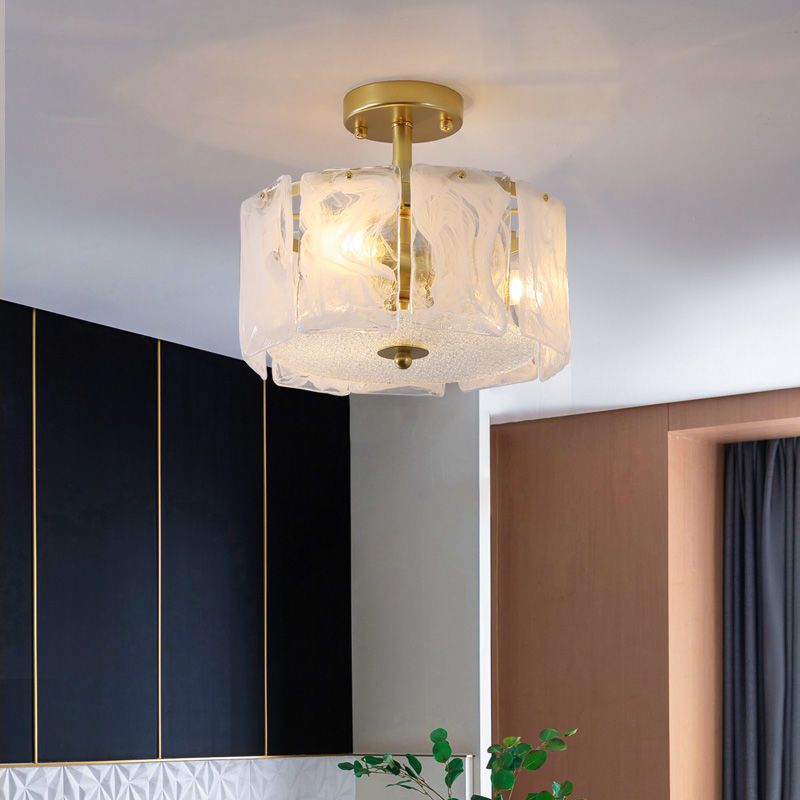 Kirsten glass-panel light near a dark wall with gold lines, geometric lower panels, wood-toned opening, dark curtain and leafy plant.