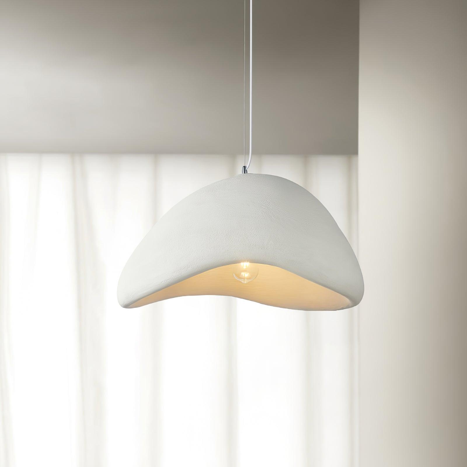 Close-up White textured cloud pendant with a pale cord, flowing lower edge and round glowing bulb before curtains