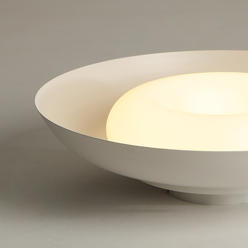 Close-up of the white bowl rim and luminous convex centre, with the ceiling plate resting below on a pale surface.