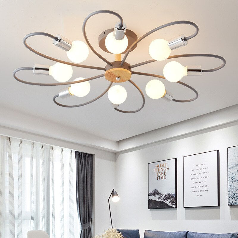 Gray eight-head flower ceiling light with silver-tone holders glowing above a sofa beside windows and framed prints