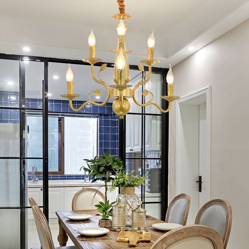 Gold 6-Light Marilyn above a wood dining table with white plates and green foliage, beside a black-framed glass partition.