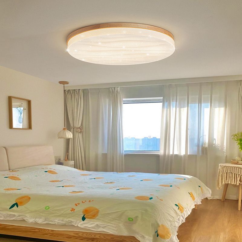 Round Ozawa ceiling light with a rippled white face and wood-tone rim above fruit-pattern bedding, a wood bed base and pale curtains.
