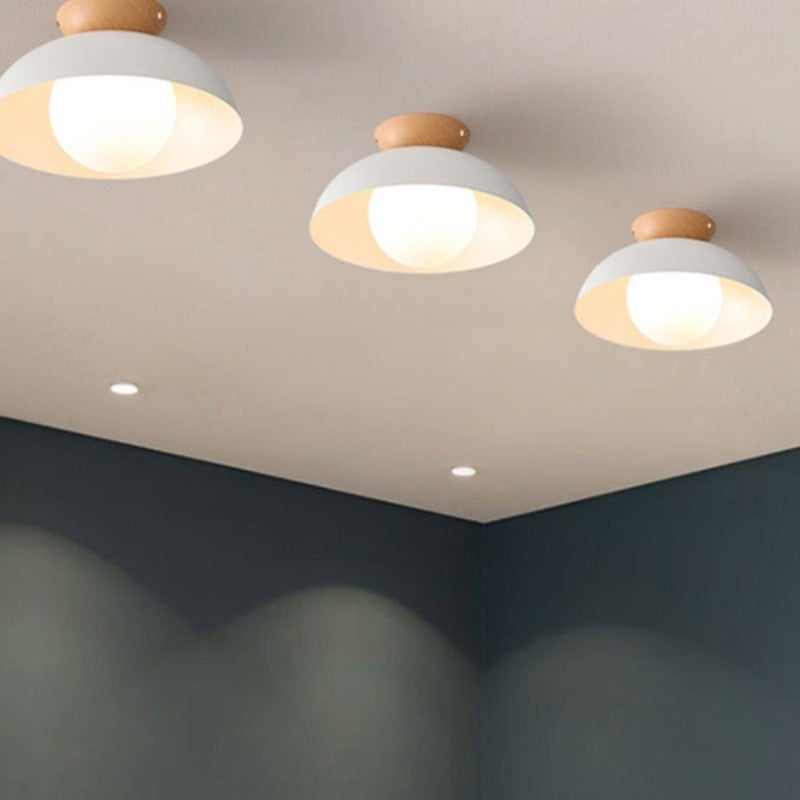 Three lit white dome ceiling fixtures with wood crowns and projecting white globes across an indoor ceiling
