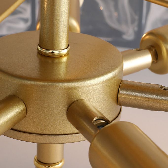 Close-up of Kirsten gold-toned central hub and radial arms, with partial bulb holders, glass panels and rails behind.