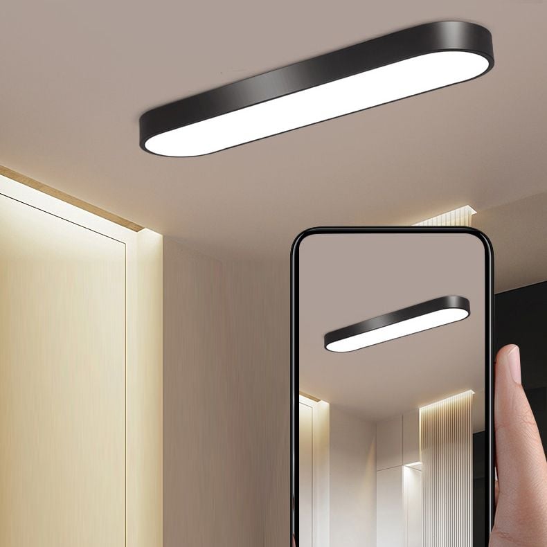 Black Quinn ceiling light above light wood panels, with a hand holding a phone whose screen repeats the room photograph.