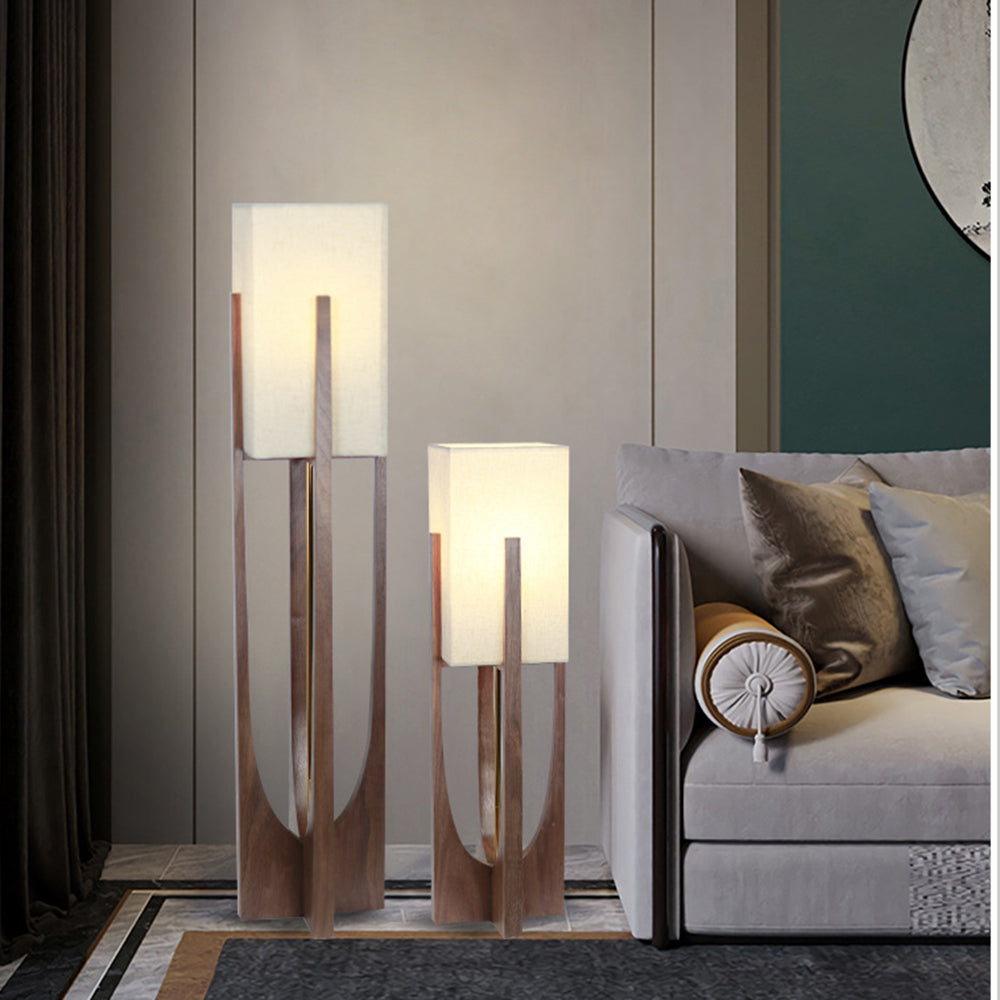 Two walnut-tone Ozawa lamps of different heights beside gray sofa, cream and metallic cushions, paneled wall and dark curtains