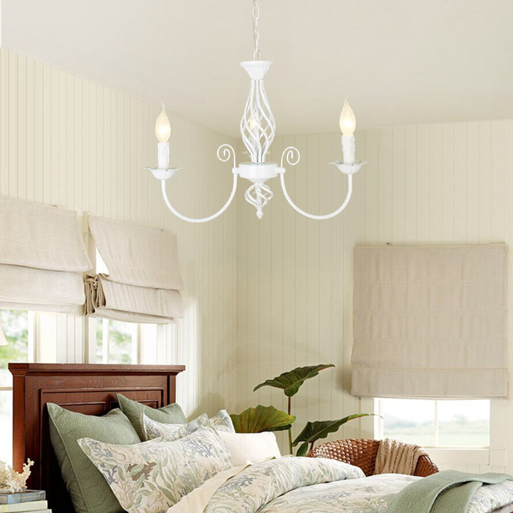 White Silva three-light chandelier above bed with pale patterned bedding, roman blinds and plant, showing central glow