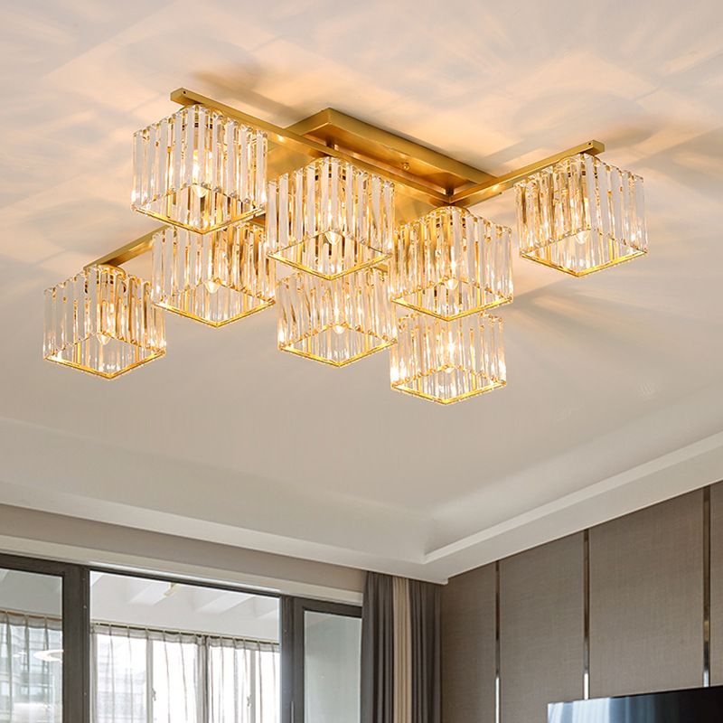 Eight gold-toned Kristy cube shades near a dark-framed window, sheer and grey curtains, brown wall panels and partial TV.