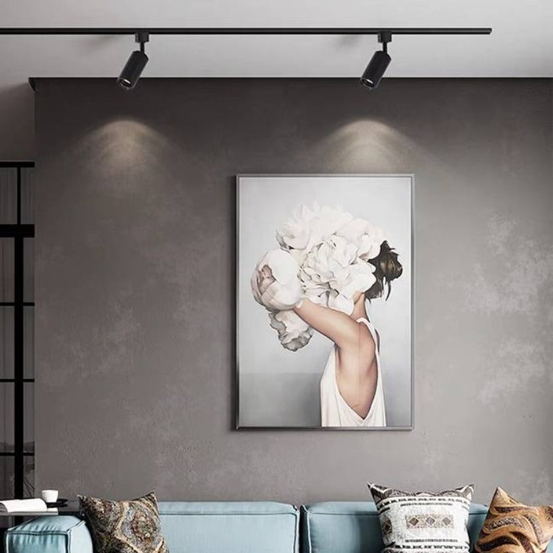 Black Freja two-head track casting wall light pools above a flower-covered portrait and teal sofa cushions against a grey wall.