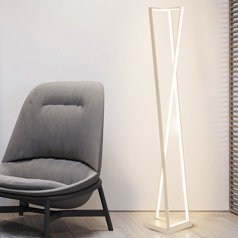 White crossed-triangle floor lamp beside a grey padded chair and window blinds on a wood floor