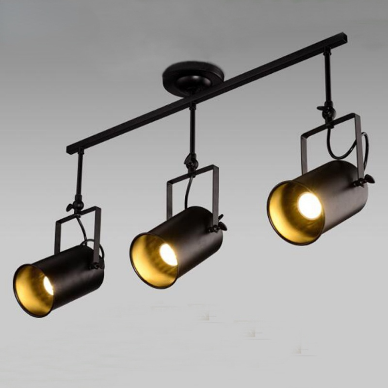 Low-angle view of Alessio three-head bar with lit cylindrical heads, gold-looking interiors and squared brackets.
