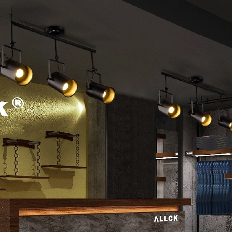 Repeated Alessio three-head bars above yellow wall panel, chain-hung wood shelves, long ledge and blue quilted display items.