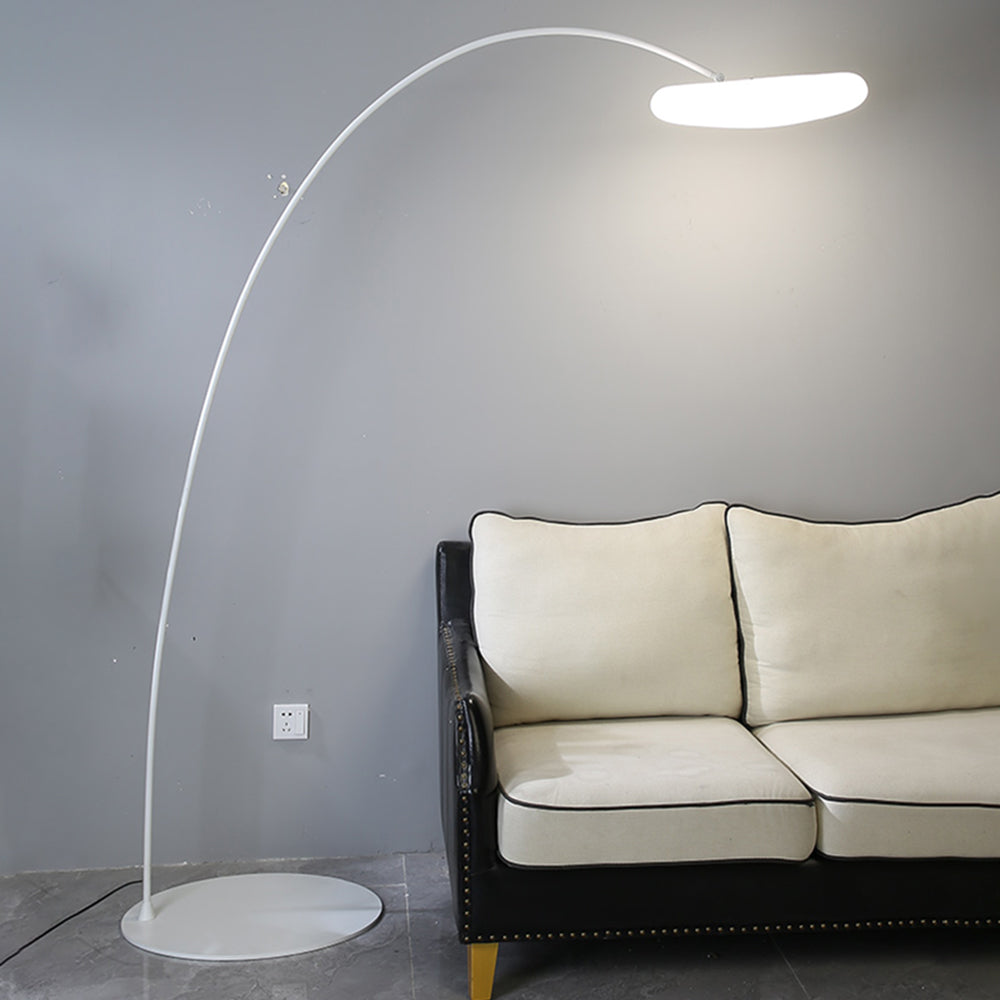 White Minori arc lamp lit beside a sofa against a grey wall.