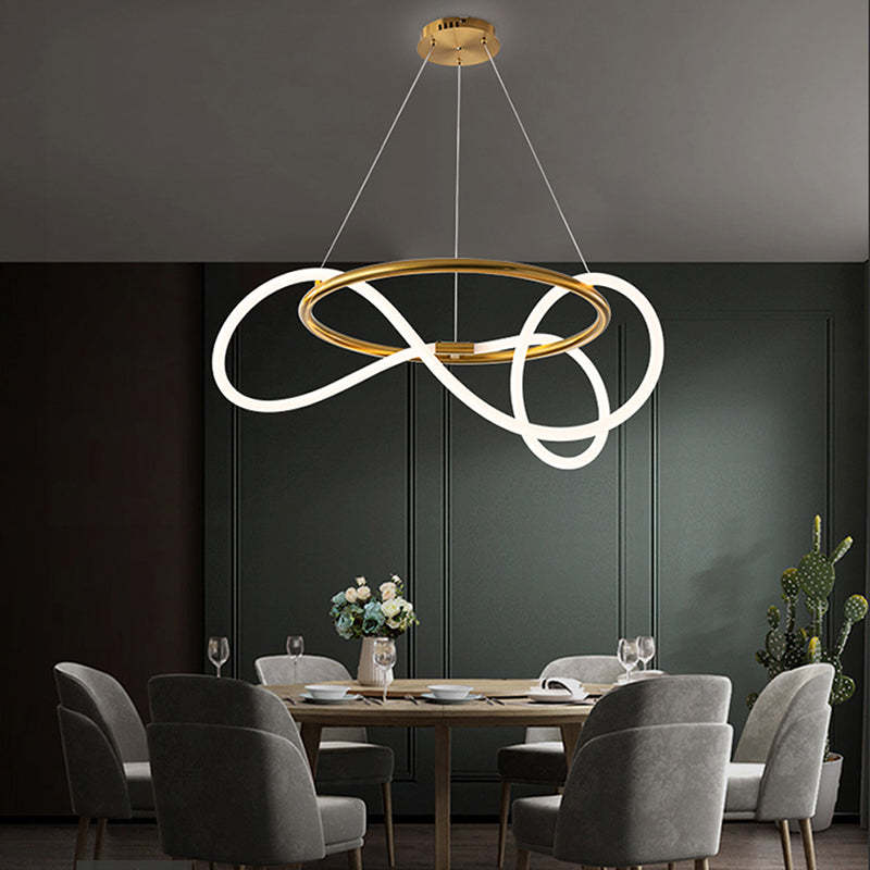 Gold Louise ring with crossing luminous loops above a wood dining table and gray chairs, with flowers, glasses and a cactus.