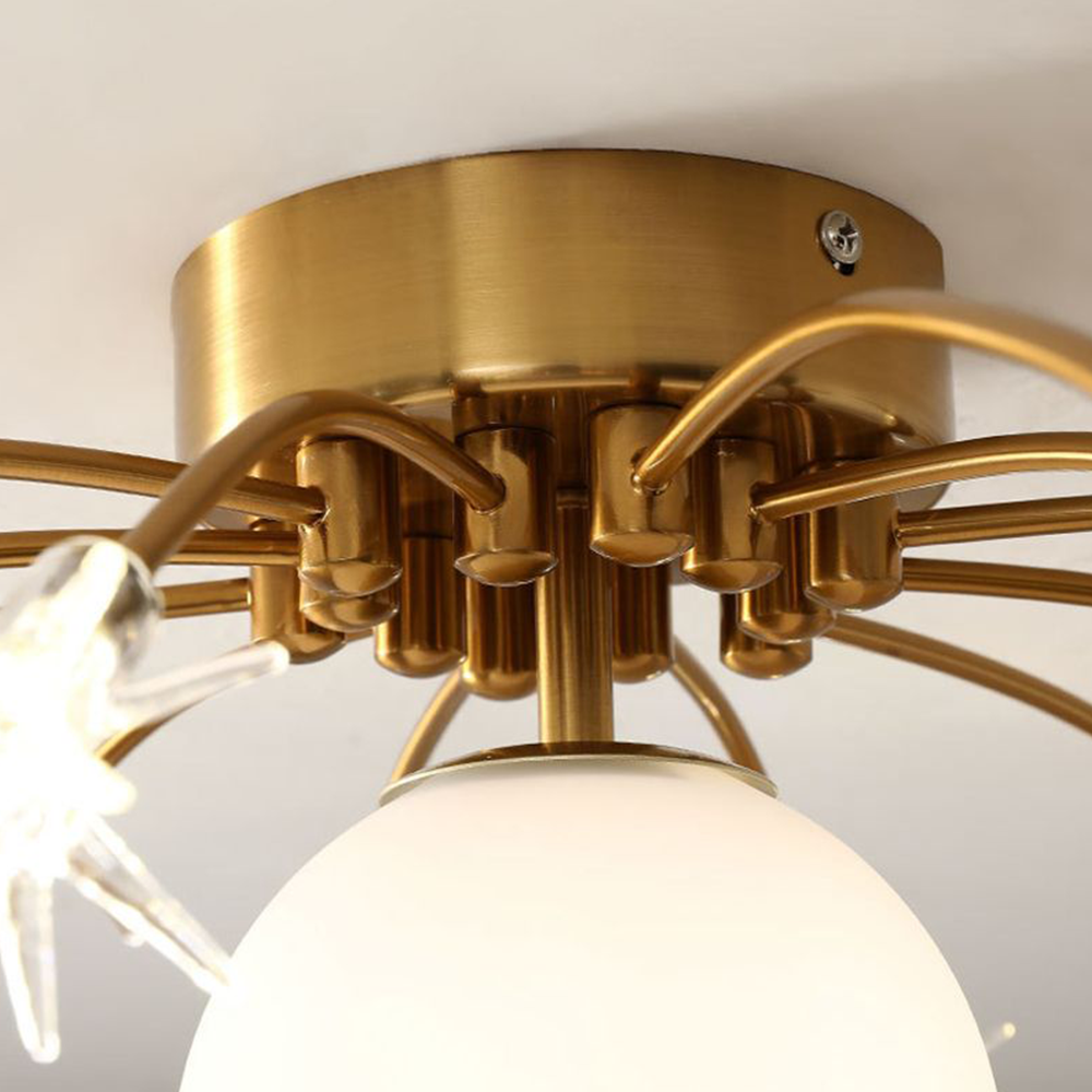Elif close-up of its gold-toned circular canopy, curved arms and holders, with a pale glass globe and clear star-shaped detail.