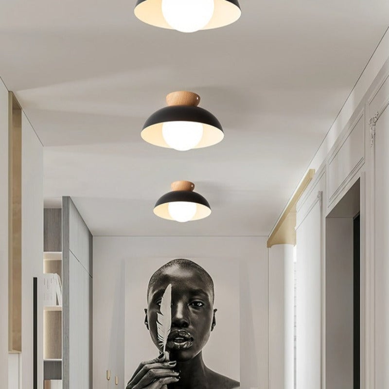 Three black wood-crowned ceiling lights along an indoor corridor, with the nearest partly cropped and a framed portrait below